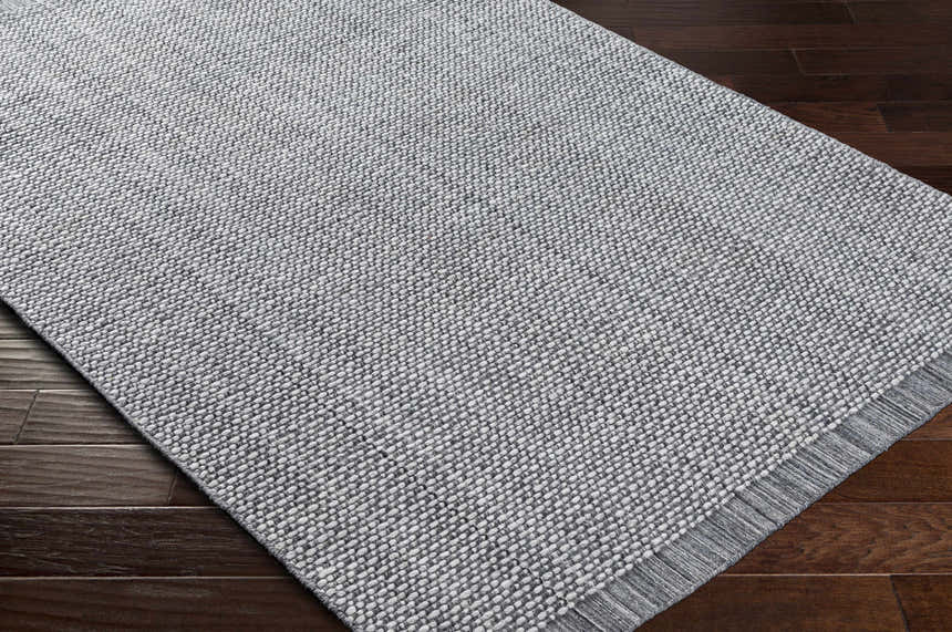 Close-up of a hand loomed light gray area rug with a subtle textured pattern on dark wood floors. Clearance rug. Corner