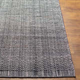 Close-up of a hand loomed light gray area rug with a subtle texture on a wood floor. Front