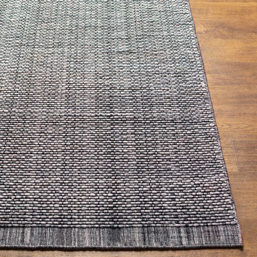 Close-up of a hand loomed light gray area rug with a subtle texture on a wood floor. Front