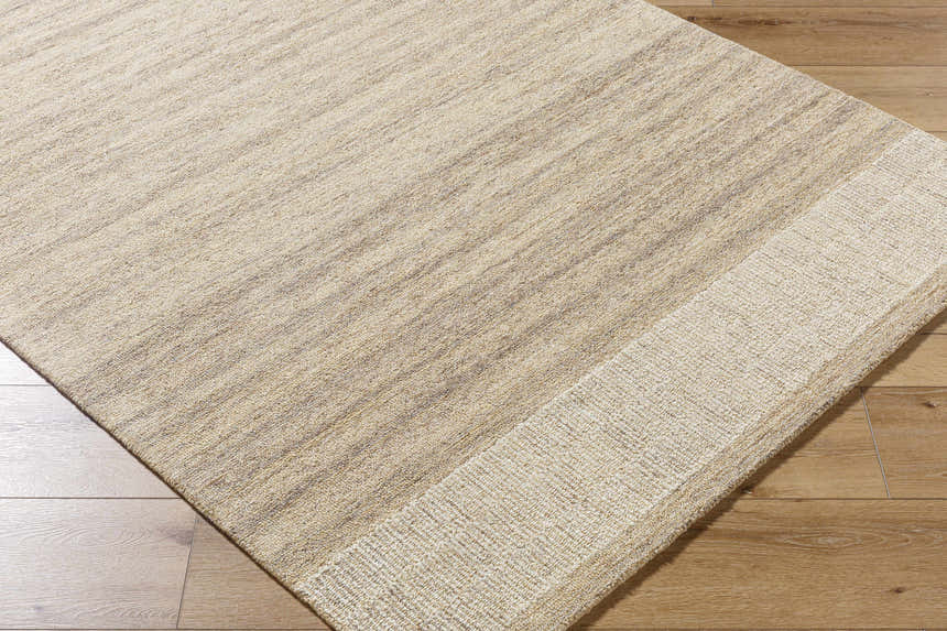 Close-up of the hand-tufted Yosef Area Rug. Prairie dust, tan, and warm gray wool rug with a subtle striped pattern. Corner