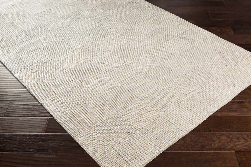 Close up of the hand woven Yarrabilba Area Rug in off white with a subtle geometric pattern on dark wood floors. Corner