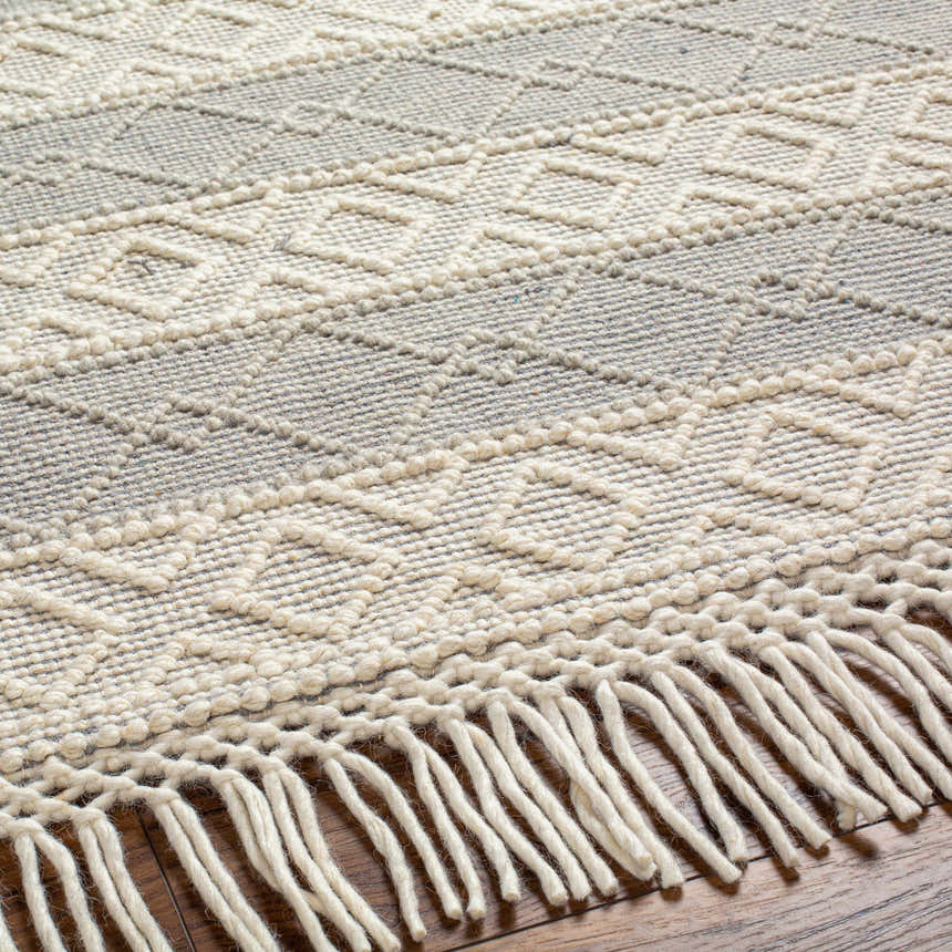 Close-up of Zaza Wool Rug with Tassels. Bone and cloud gray geometric pattern, hand woven texture, and fringe detail. Texture