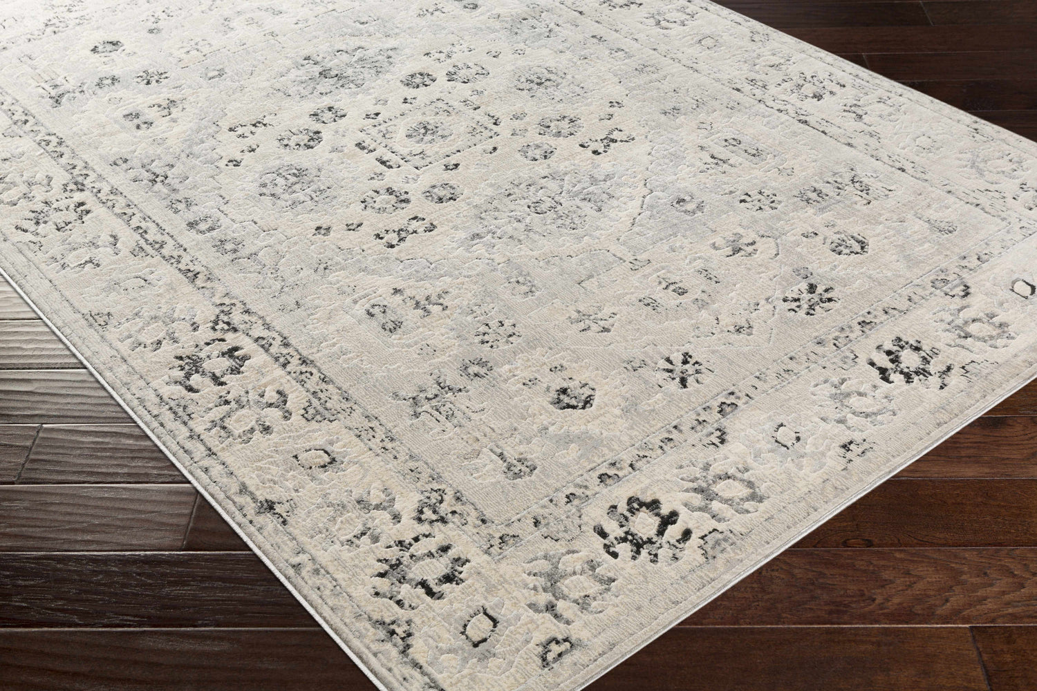 Close-up of the Zephyr Area Rug showing its farmhouse style, black, charcoal, and taupe floral pattern, and soft texture. Corner