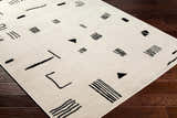 Close-up of the Zale Area Rug. Bone rug with a black geometric pattern on dark wood floors. Corner