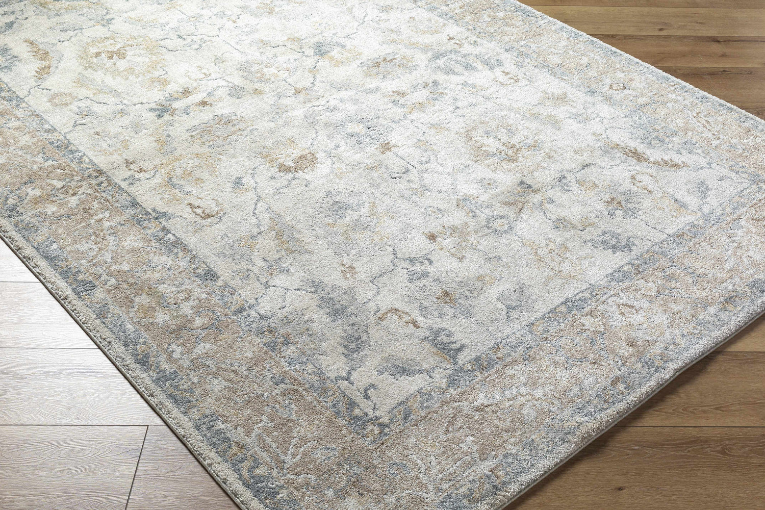 Close-up of the Uriel Thick Luxe Rug. Beige, gray, and tan traditional pattern on a machine woven rug. Corner