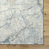 Close up of the Urowo Light Gray rug showing abstract pattern, cream, gray, light blue, and tan colors on wood floor. Corner