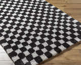 Close-up of the Zveha Area Rug. Black, light silver, and gray microfiber rug with a checkerboard pattern and hand-tufted texture. Corner