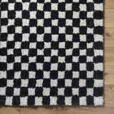 Close-up of the Zveha Area Rug. Black and light silver checkerboard pattern. Hand-tufted microfiber rug. Corner