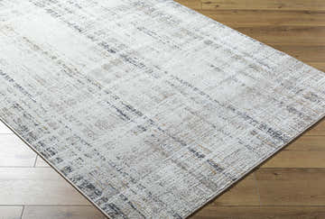 Close-up of the Zenon Area Rug showing its charcoal, light brown, and white abstract pattern on wood floors. Corner
