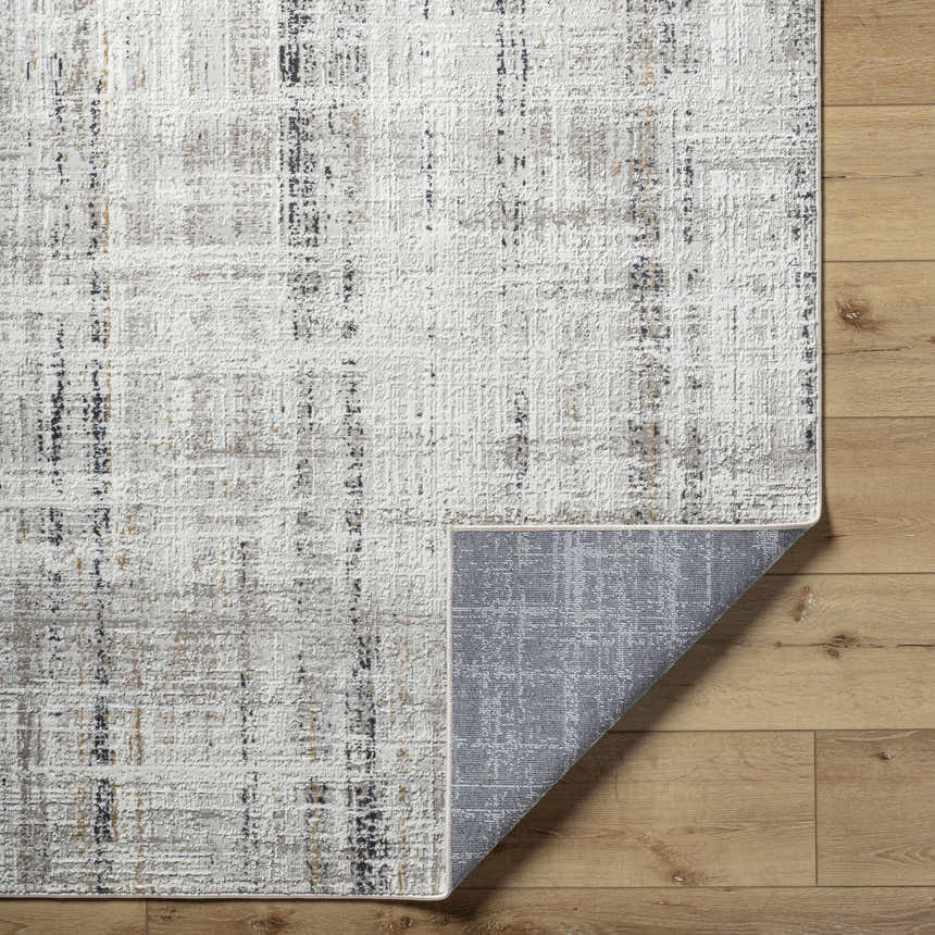 Close-up of the Zenon Area Rug showing its charcoal, light brown, and white abstract pattern and gray backing. Fold